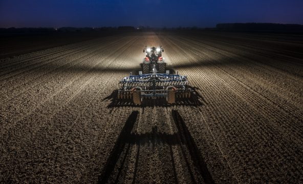 Tractor pulling cultivator through a field during the night