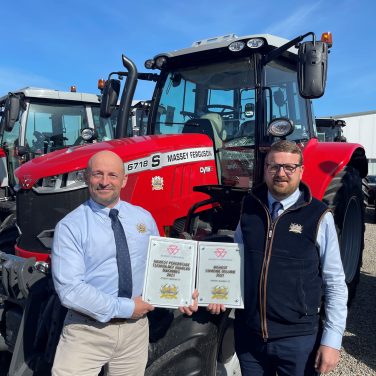 Two members of staff posing next to a tractor